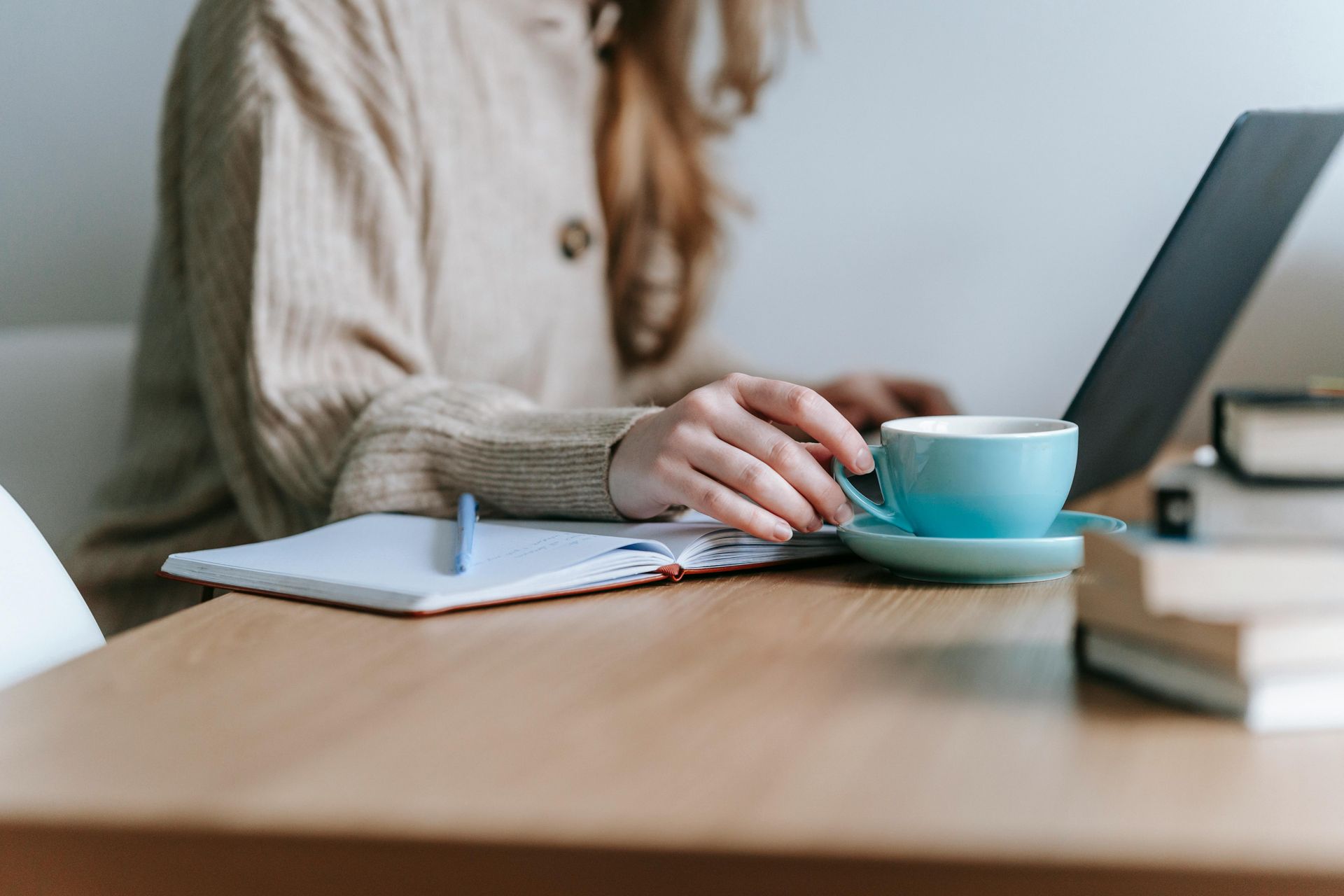 Person working on a laptop at a table with a notebook, pen, and coffee cup. Person working on a laptop at a table with a notebook, pen, and coffee cup.