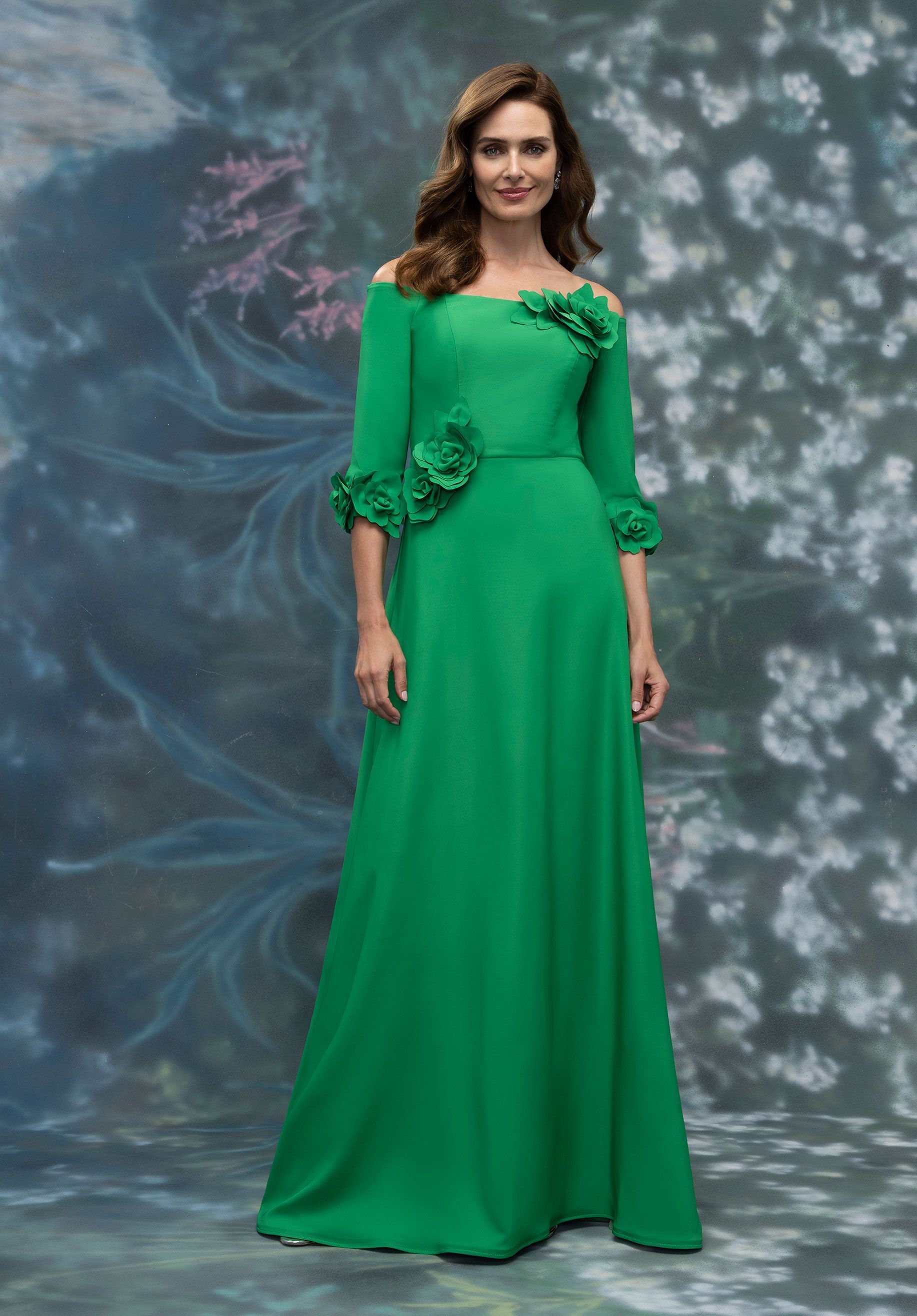 Woman in a black evening gown with floral embellishments, smiling, standing in front of white draped fabric.