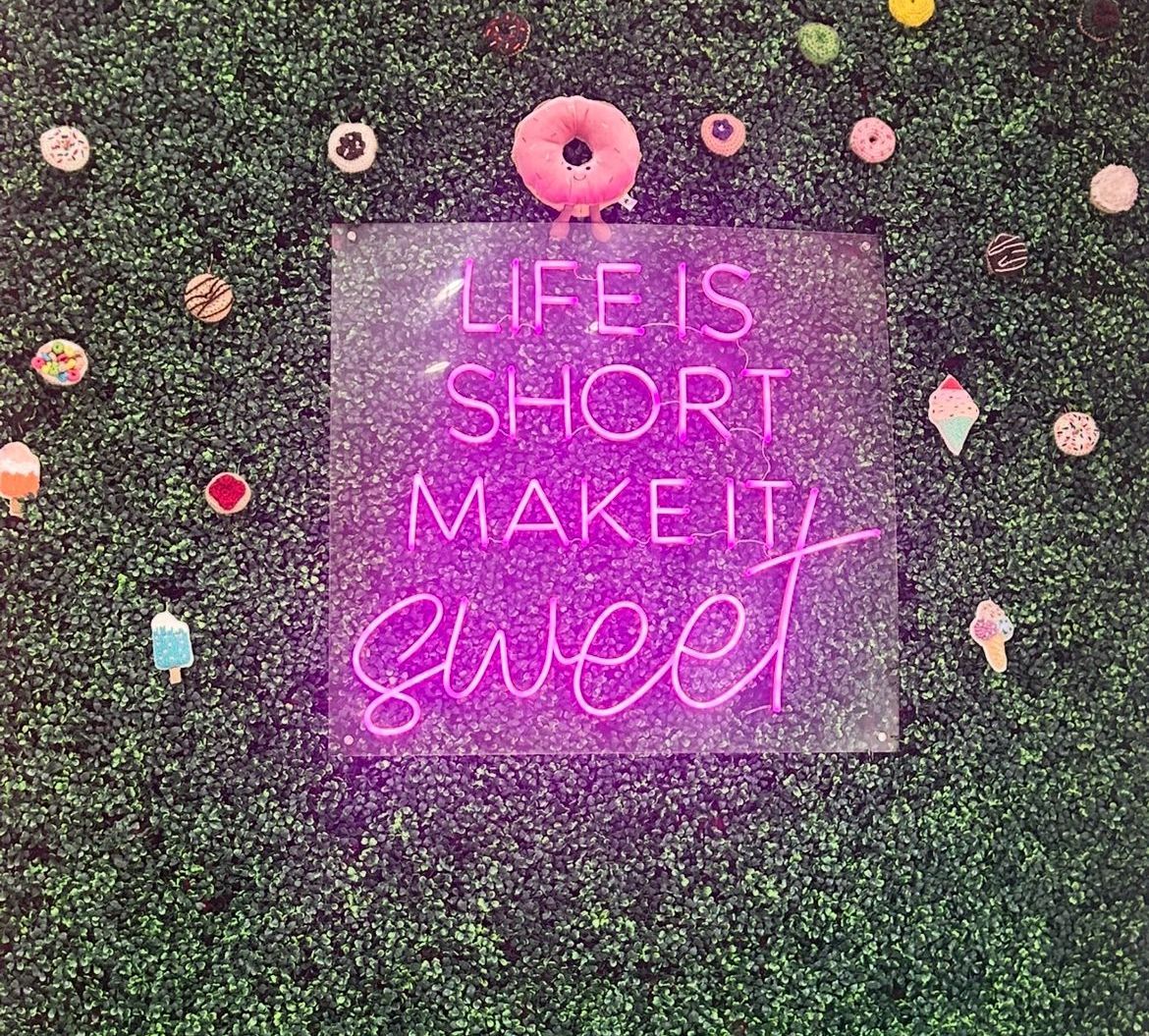 A neon sign that says `` life is short make it sweet '' is on a wall.
