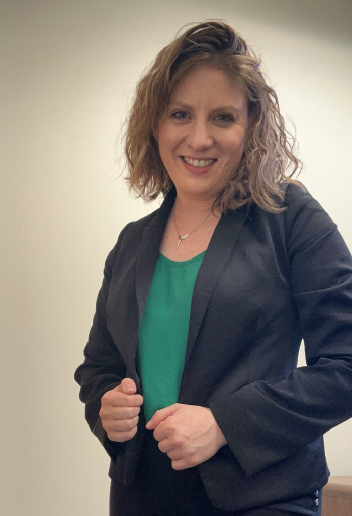 A woman wearing a black jacket and a green shirt is smiling for the camera.