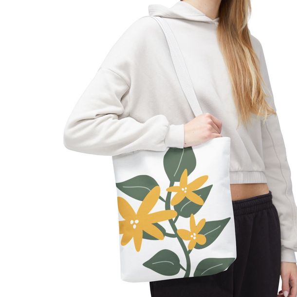 A woman is holding a white tote bag with yellow flowers and green leaves on it