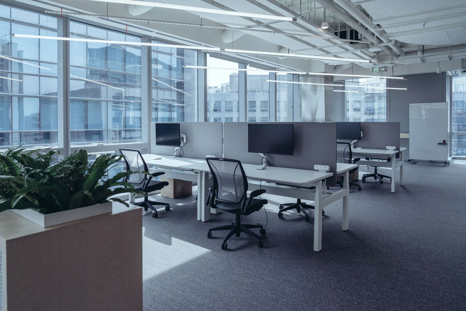 Modern office space with desks, chairs, and large windows overlooking city buildings.