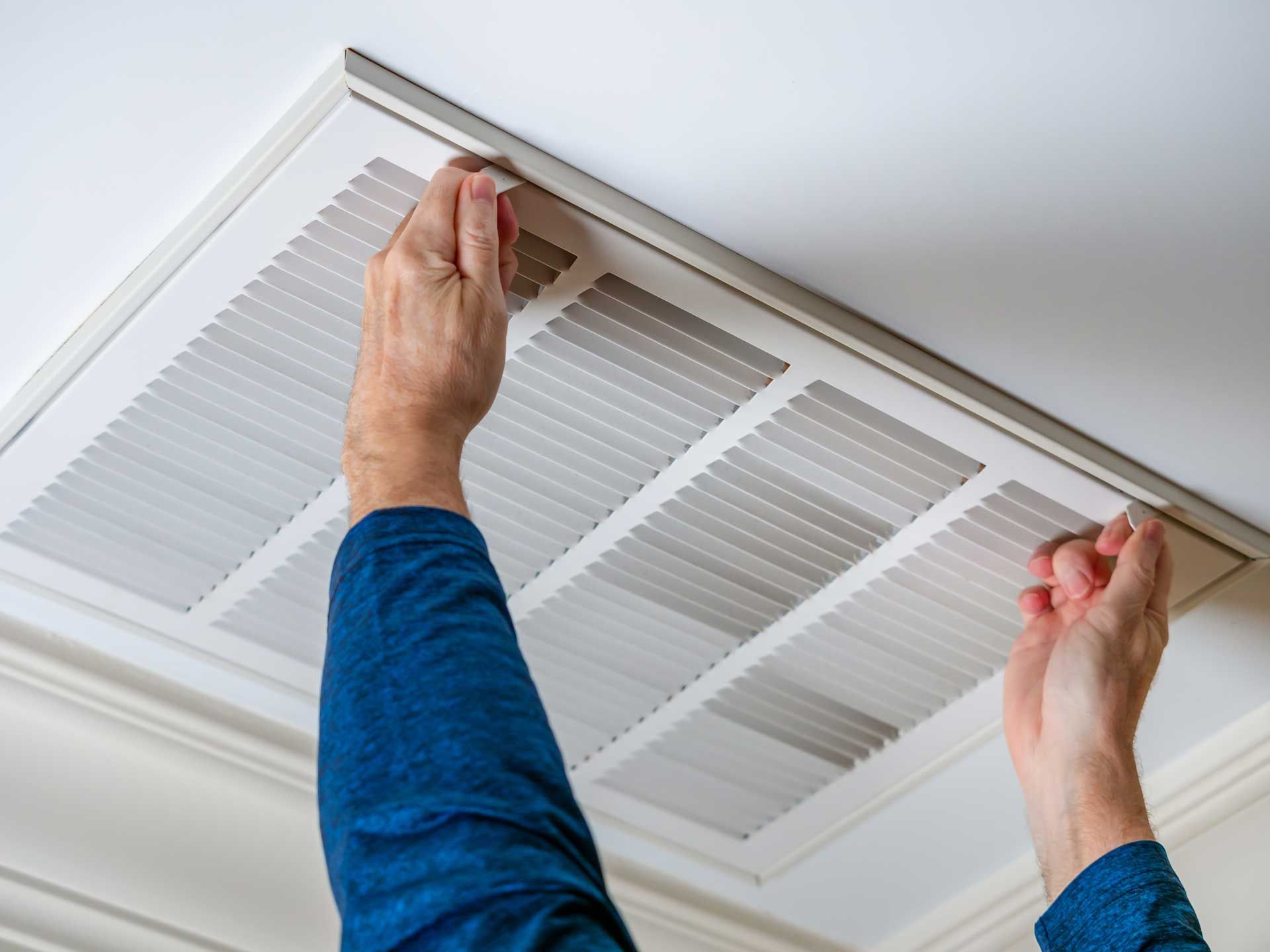 Hands removing a ceiling vent cover to access the air filter.