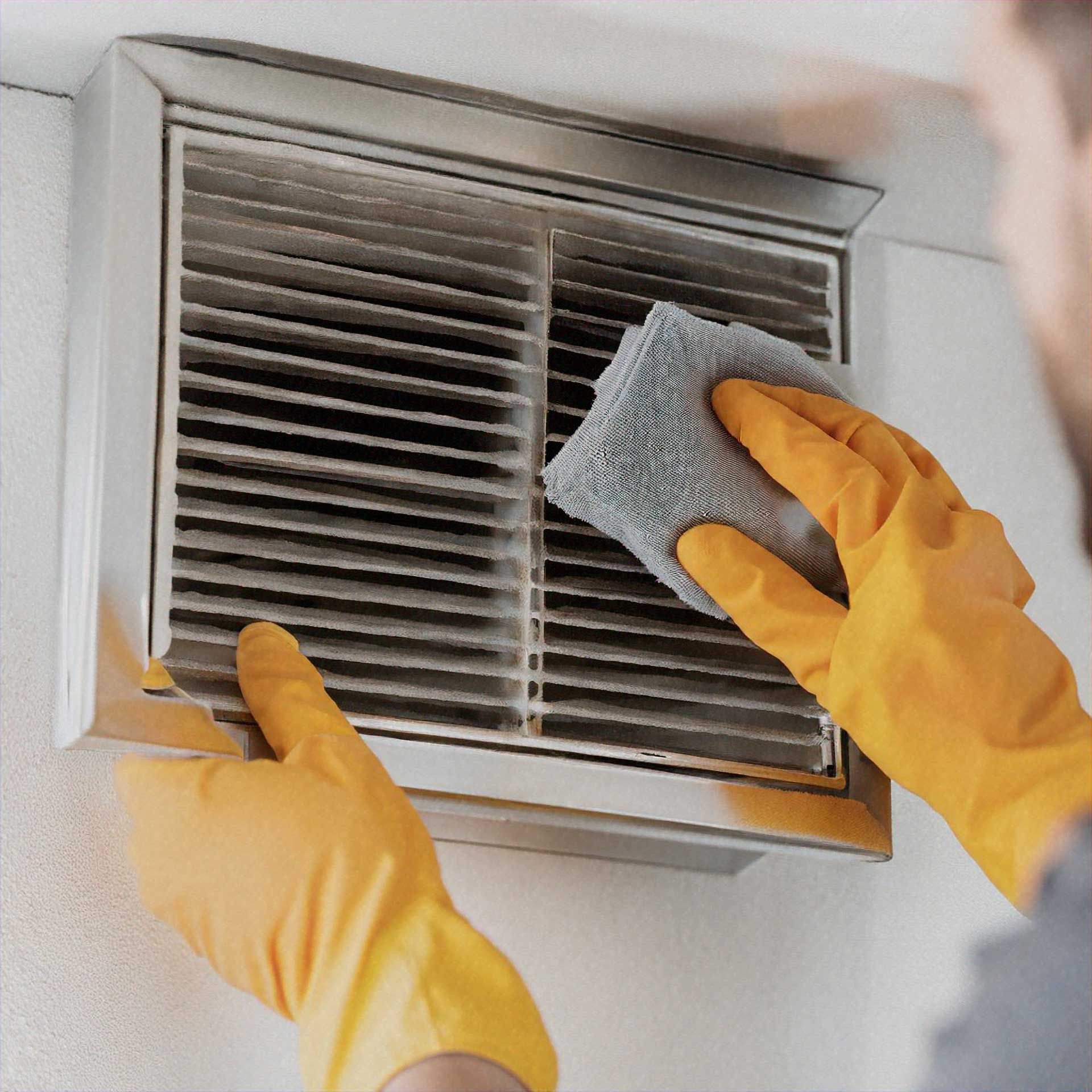 Person wearing yellow gloves cleaning a dusty vent with a gray cloth.