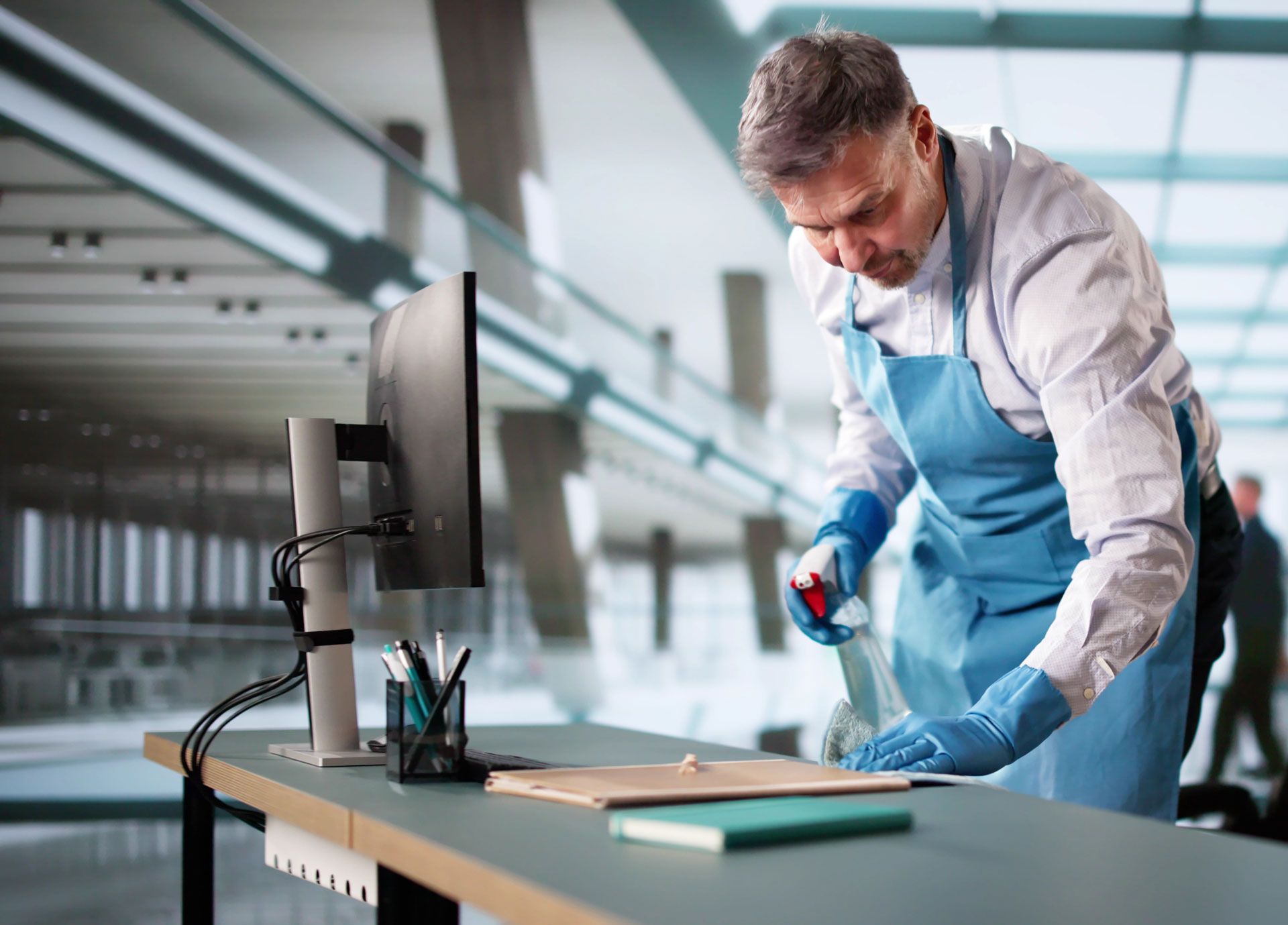 Man in apron and gloves sanitizing a desk in an office.