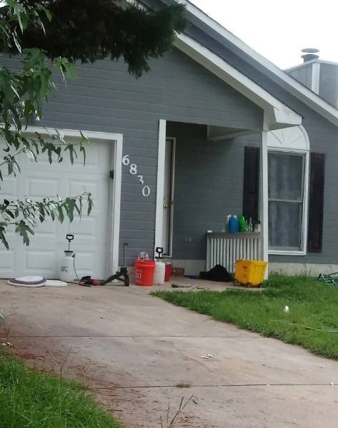 Gray house with a white garage door, open front door, and a driveway with various objects scattered on it.