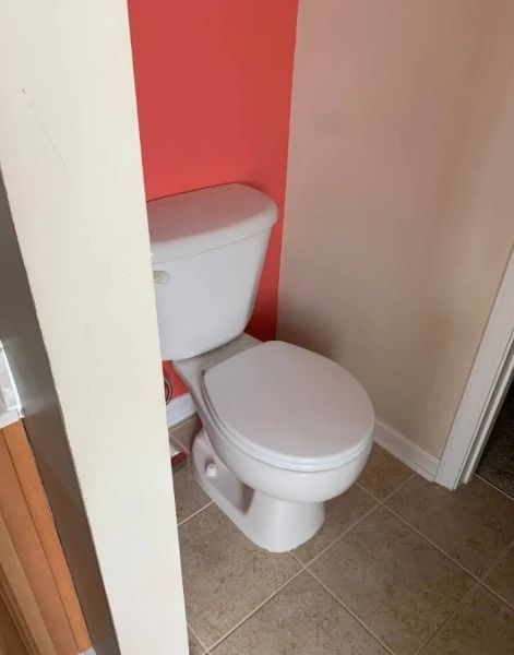White toilet in a small bathroom with coral and beige walls and tan tiled floor.
