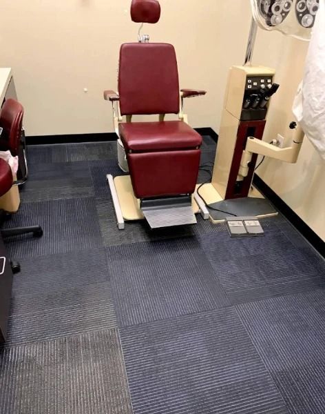 Red medical chair in a doctor's office with beige equipment and blue-grey carpet flooring.
