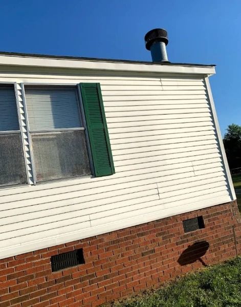 White-sided house with green shutter, brick base, and chimney against a blue sky.