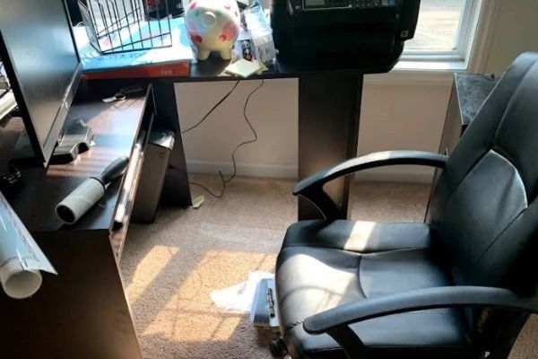 Office desk with computer, black office chair, and cluttered workspace.