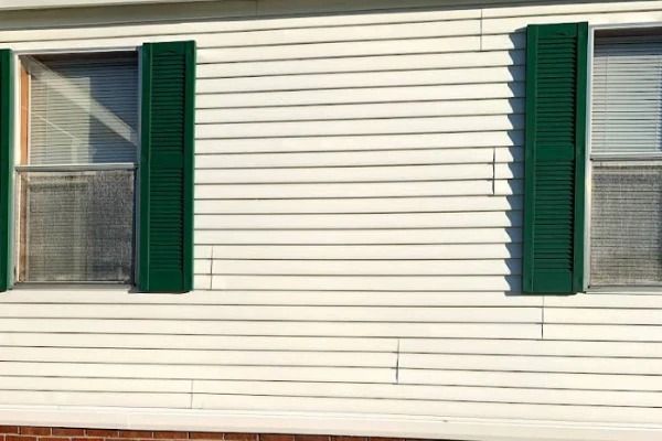 White house siding with two windows and green shutters.