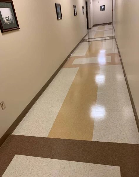 Long hallway with beige walls, patterned floor, and several framed pictures.