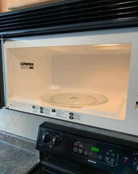 Opened microwave with a glass plate inside, above a black oven.