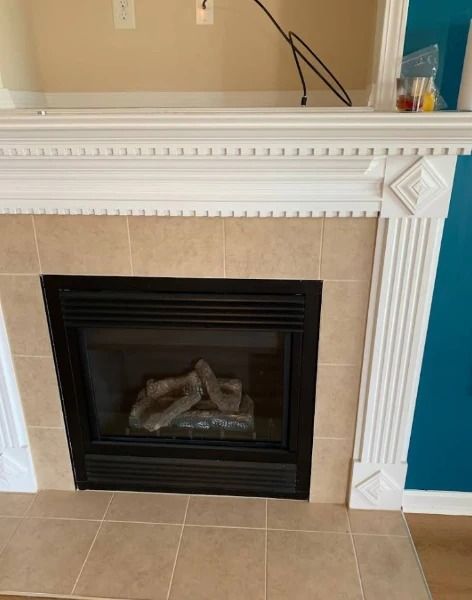 Fireplace with beige tile surround, black firebox, white mantel, and teal wall.