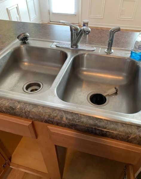 Double stainless steel kitchen sink with faucets. The sink is on a brown countertop and has wooden cabinets below.