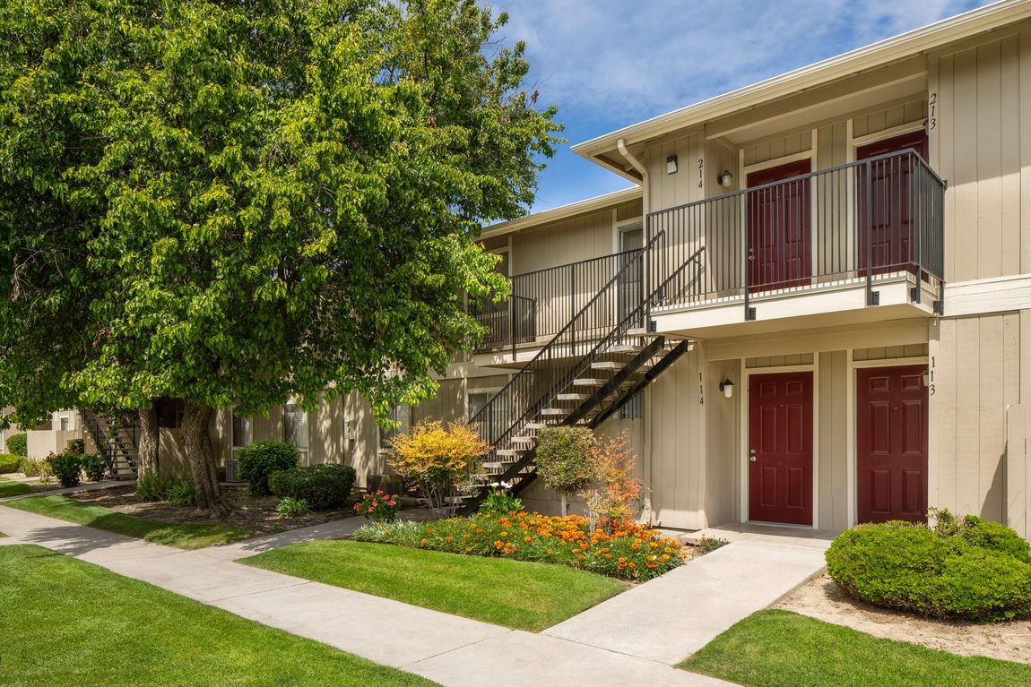 Apartment building exterior with burgundy doors, green lawn, and a tree.