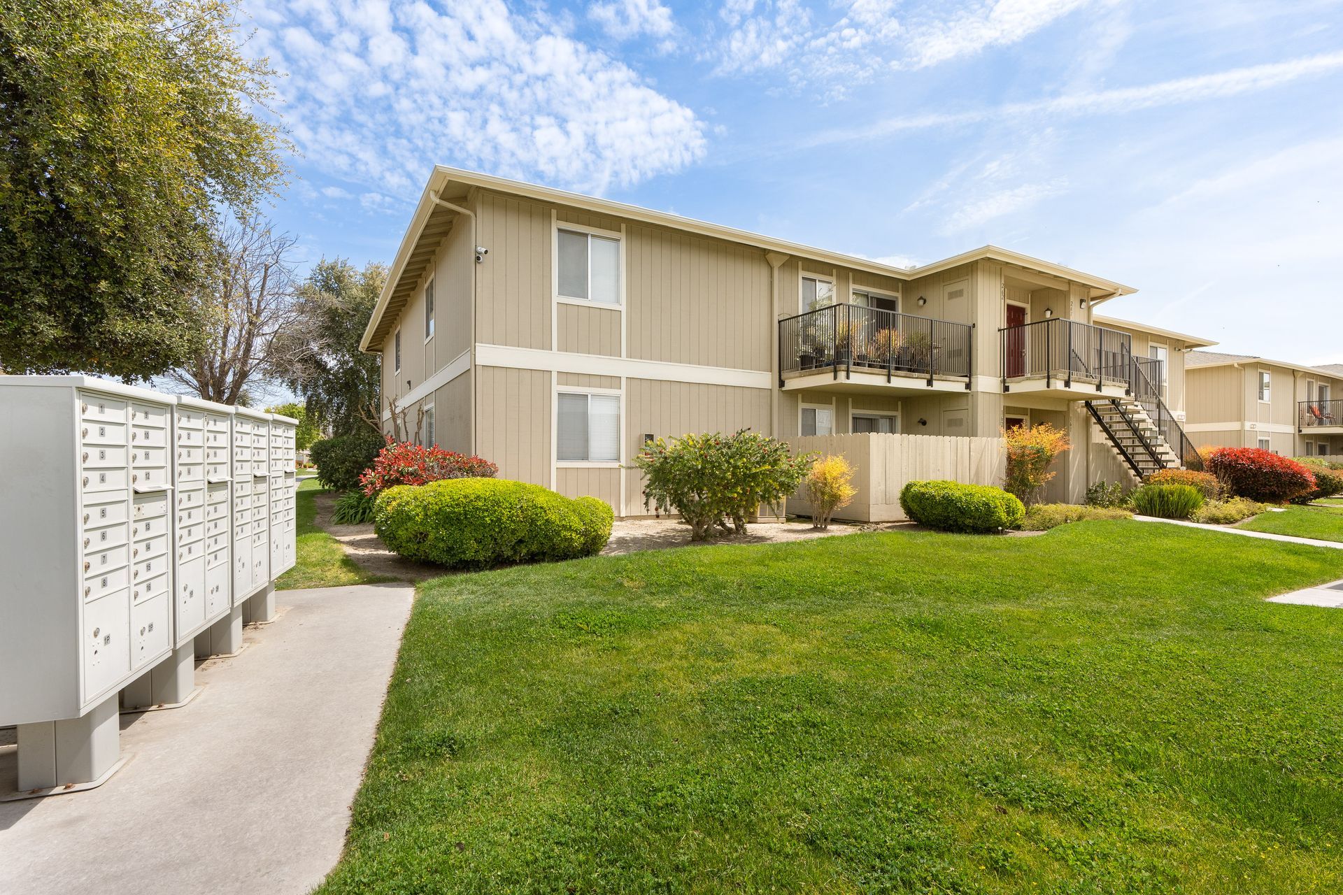 Apartment building with beige siding, green lawn, and white mailboxes under a blue sky.