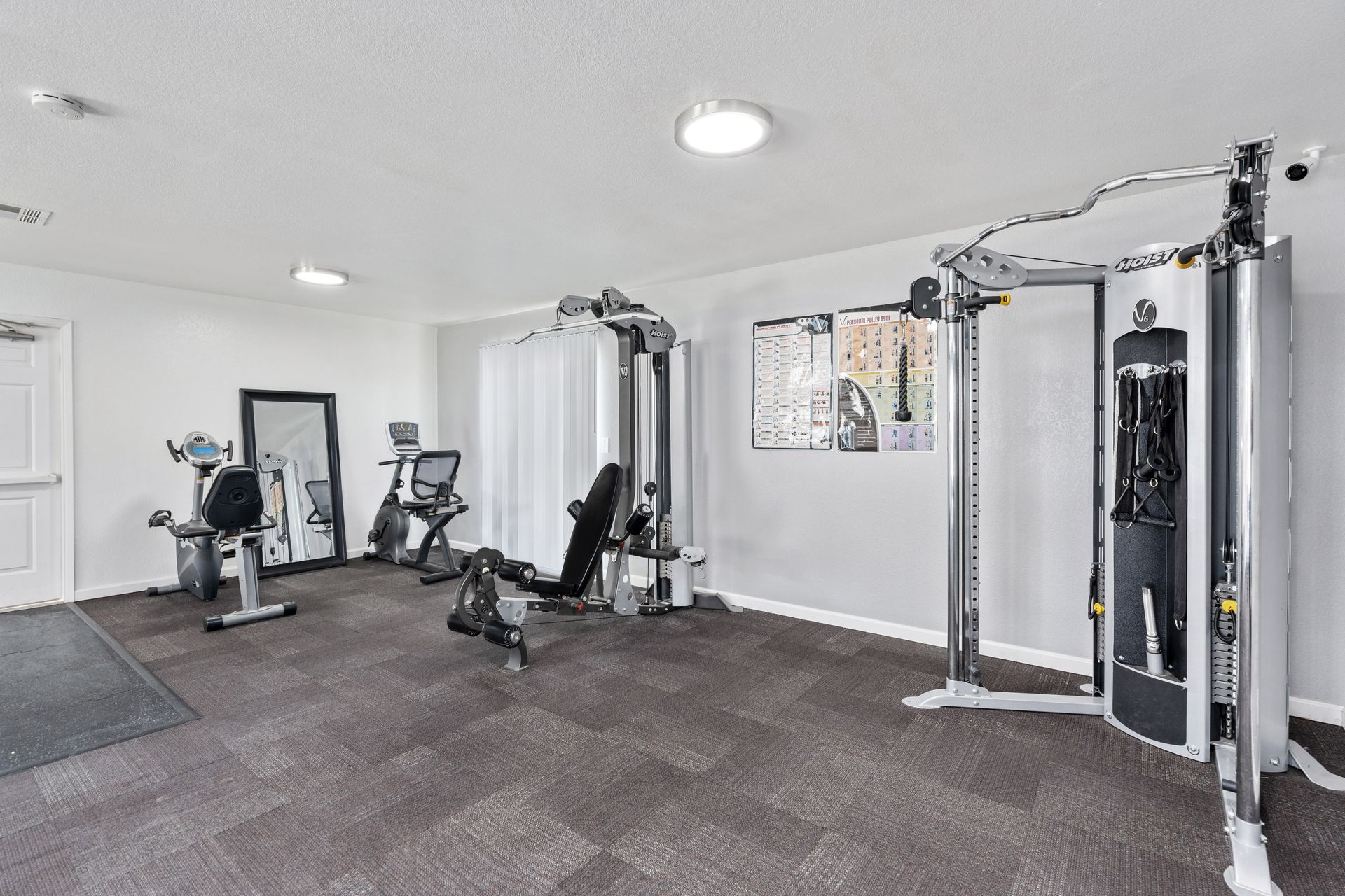 Gym with exercise machines, including a cable machine, stationary bikes, and a mirror.