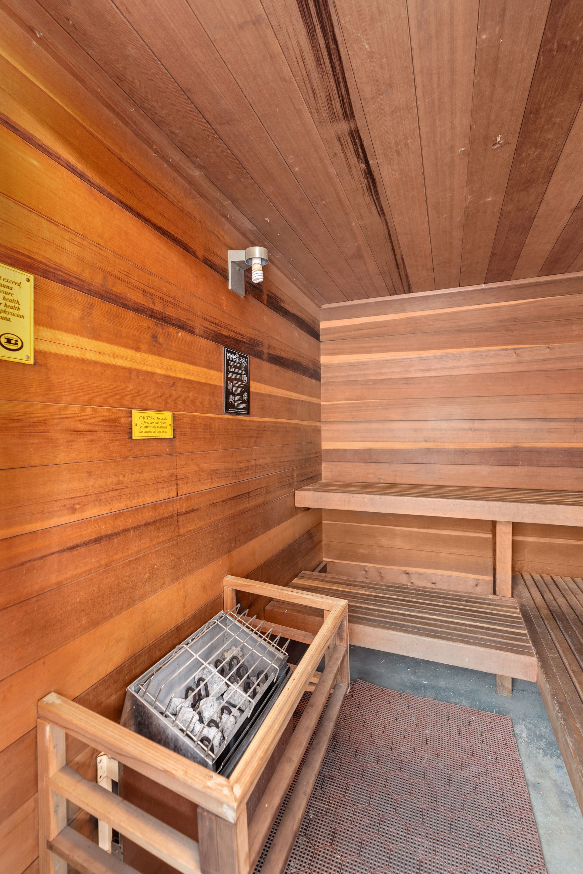 Interior of a wooden sauna with benches, a heater with rocks, and control panel.