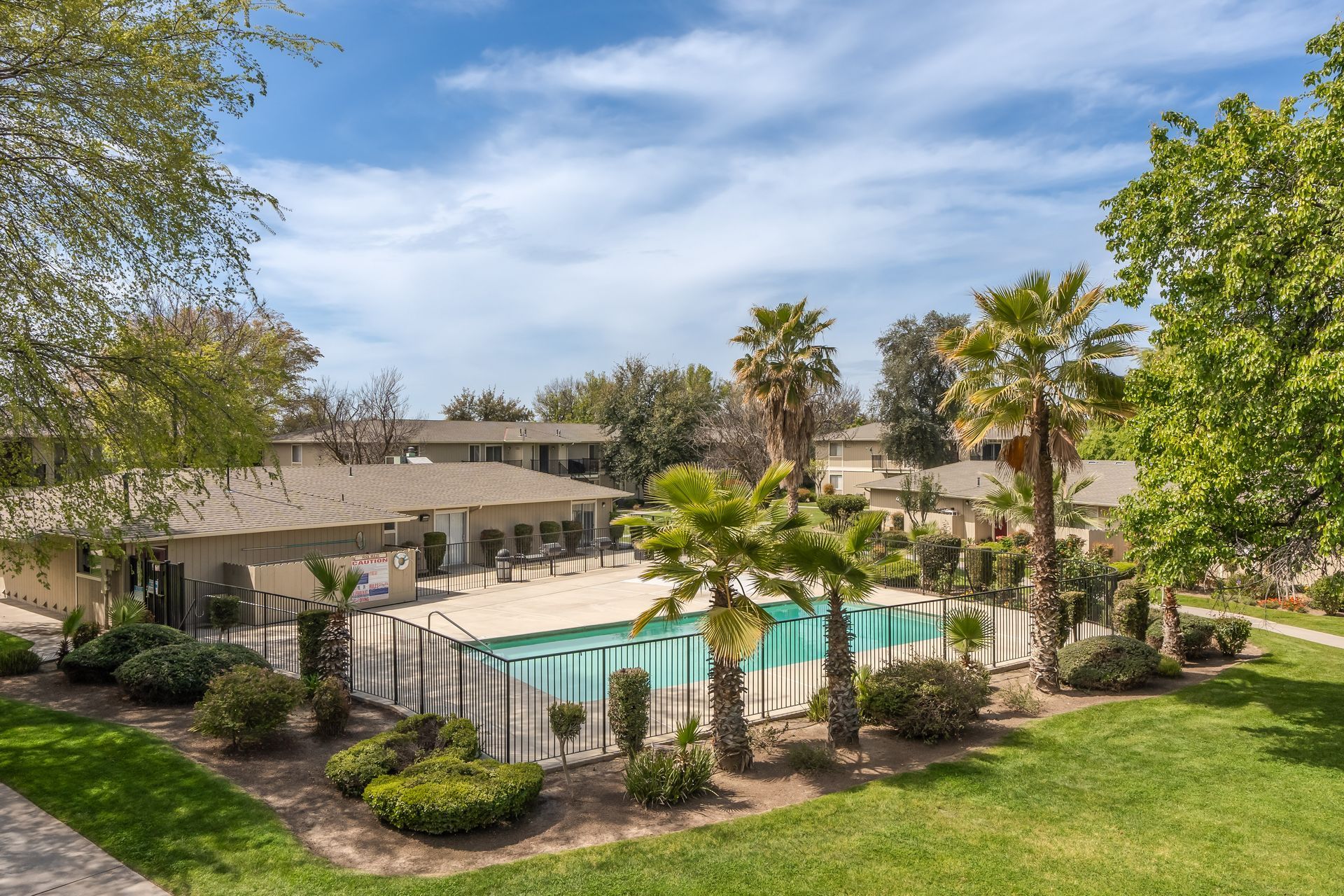 Apartment complex with pool, palm trees, and grassy lawn on a sunny day.