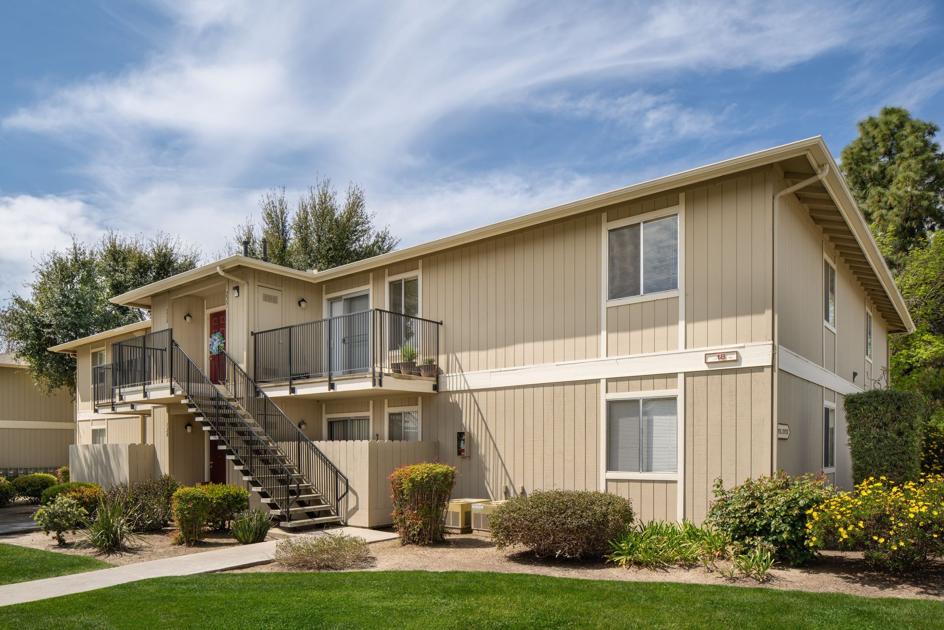 Two-story beige apartment building with stairs, grass lawn, and blue sky.