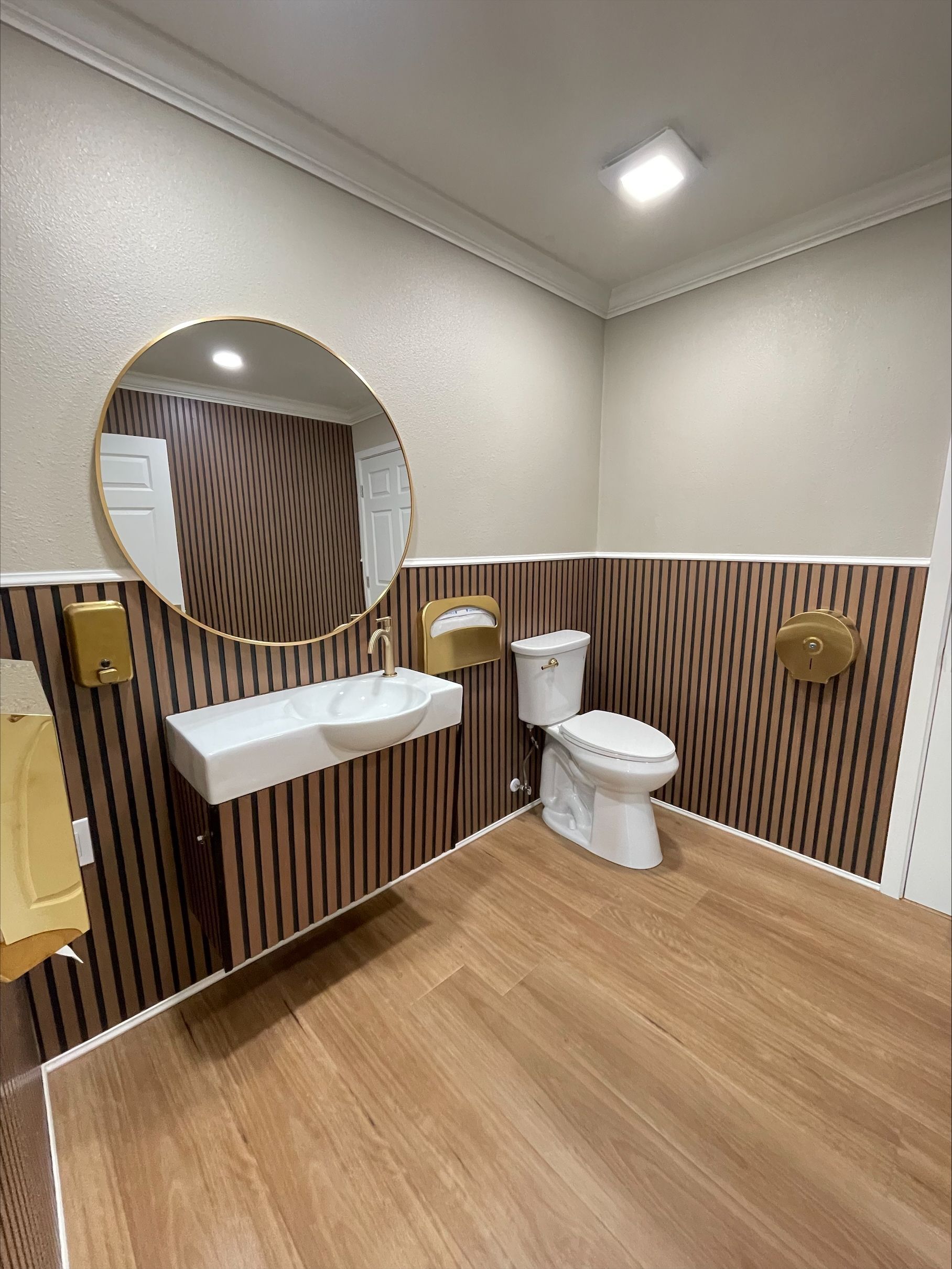 Modern bathroom with wood-paneled walls, a round mirror, a floating sink, and a white toilet.