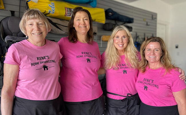 Four women in pink shirts pose together, smiling, in front of a wall with gear.