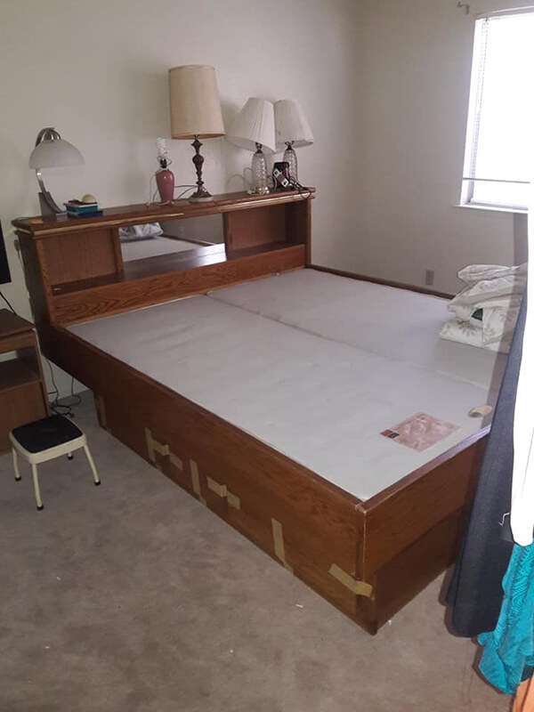 Brown wooden bed with built-in headboard, multiple lamps, and storage drawers. Located in a room with a window.