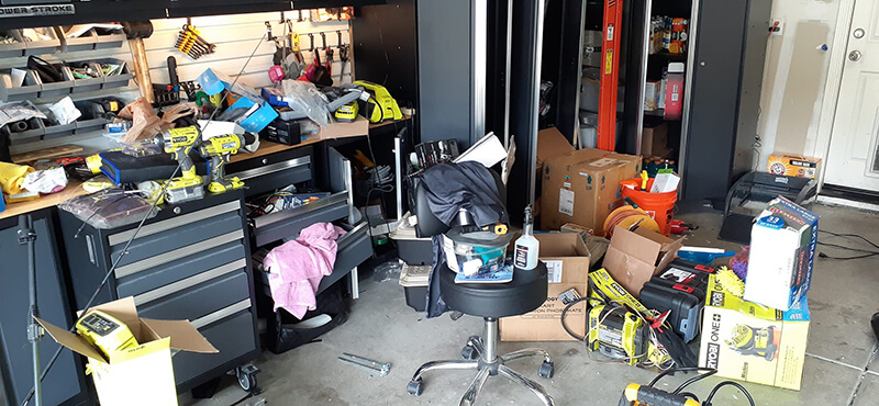 Cluttered garage with tools, boxes, and a rolling chair.