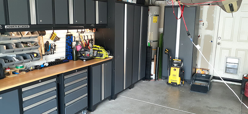 Garage with cabinets, workbench, tools, pressure washer, and garage door. Dark gray and wood tones.