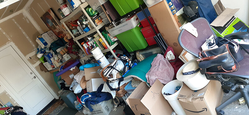 Cluttered garage with boxes, shelves, and various items. Bright green storage bins are visible.