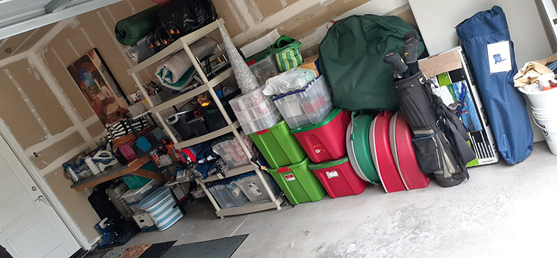 Cluttered garage with shelves, storage bins, golf bags, and other items.