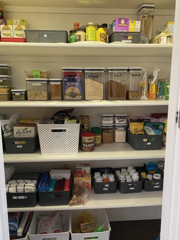 Pantry organized with shelves holding containers, baskets, and various food items. White, gray, and clear colors dominate.