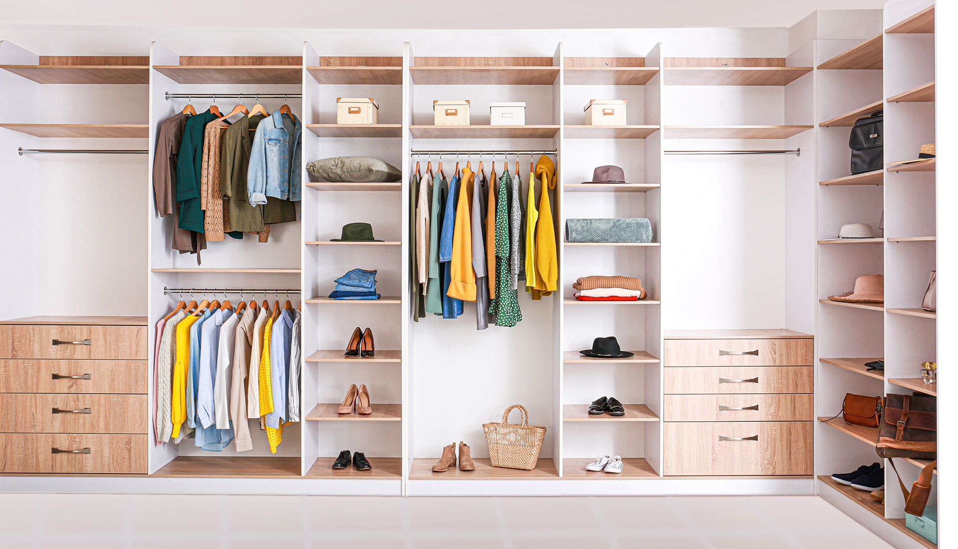 Walk-in closet with light wood shelving, hanging clothes, drawers, and folded garments.