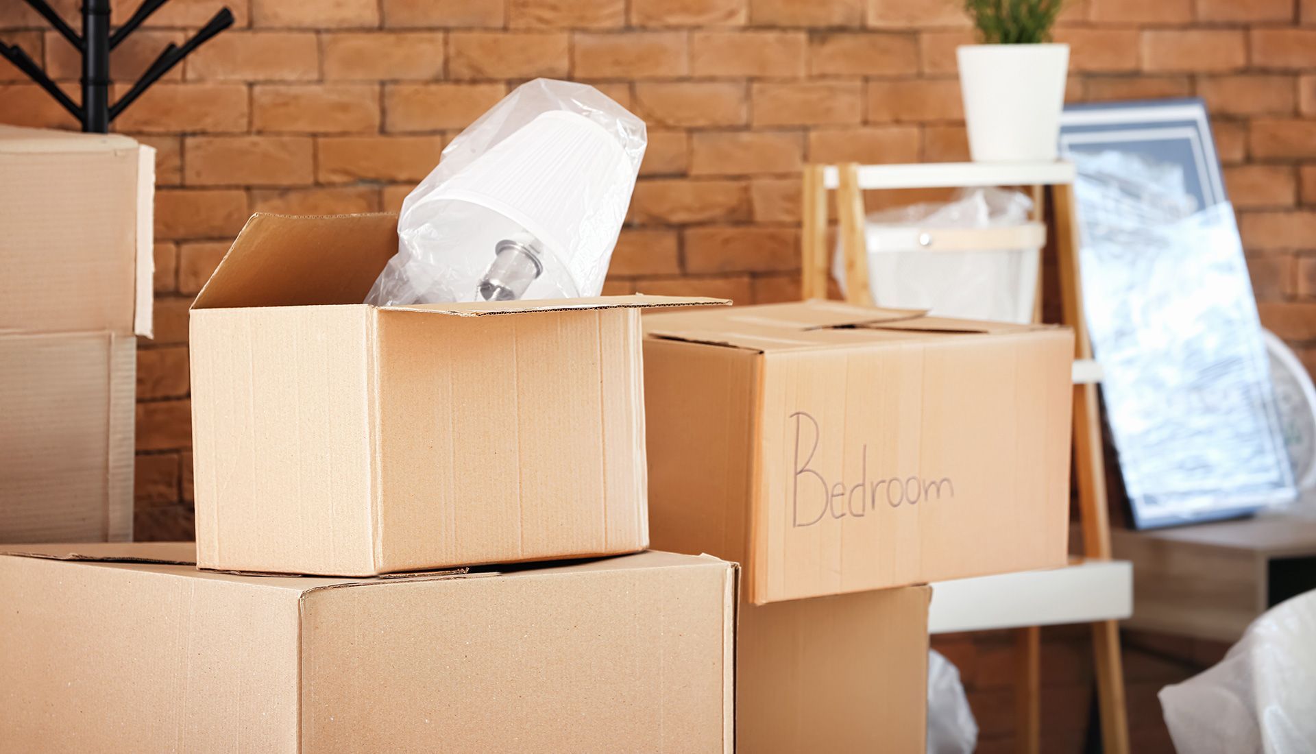 Boxes packed for a move, in a room with a brick wall. One box is open with a wrapped object inside.