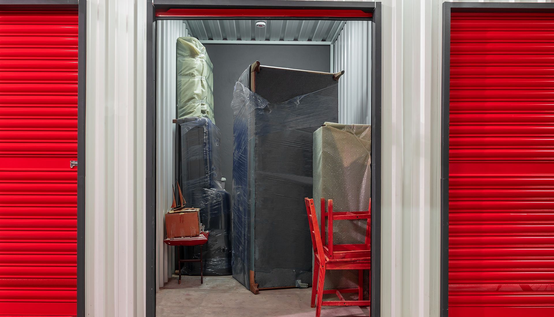 Storage unit interior with furniture wrapped in plastic. Red doors on either side.