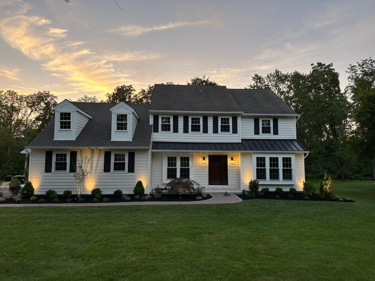 Two-story white house at dusk with lit windows and a large green lawn