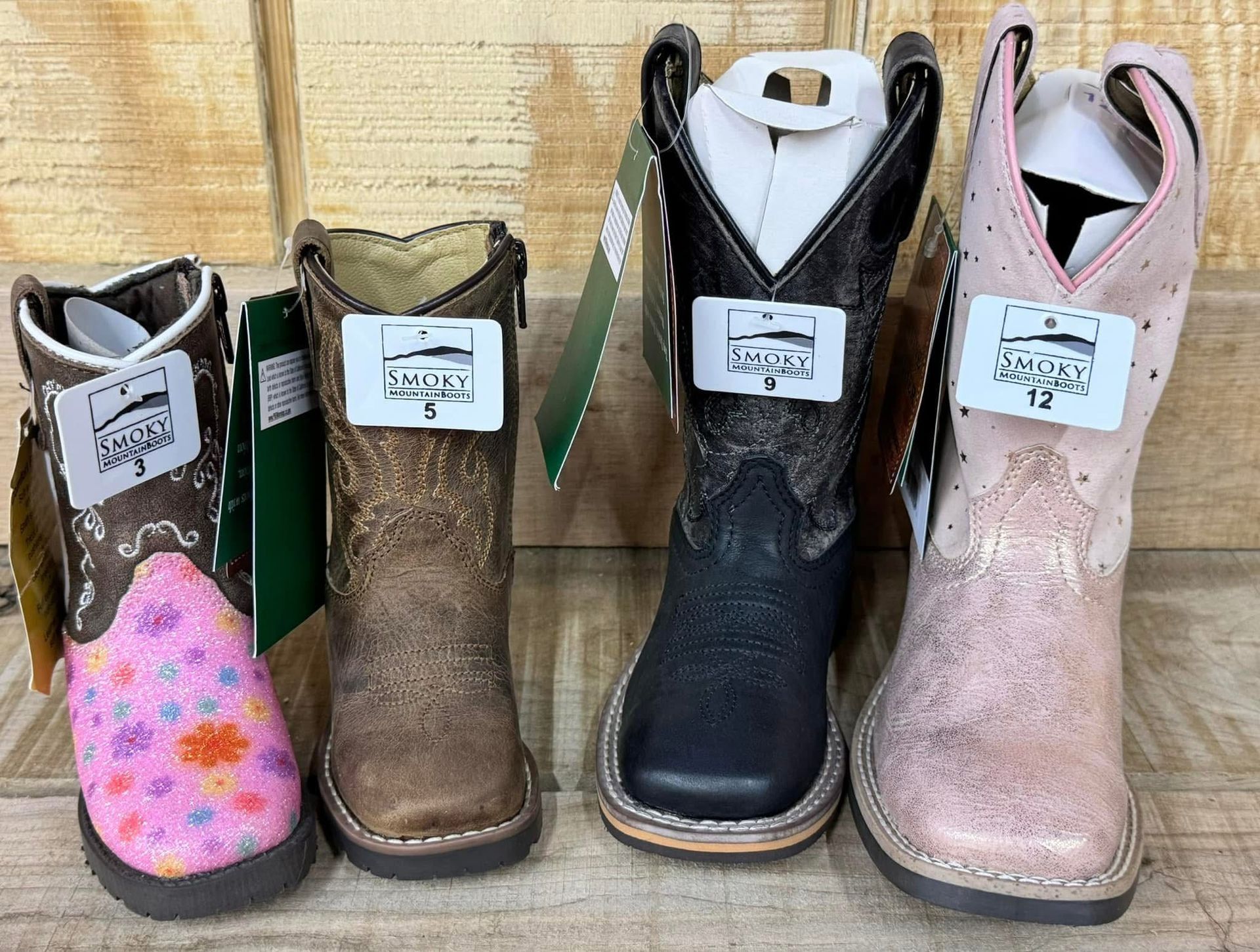 Four pairs of toddler cowboy boots are lined up on a wooden table.