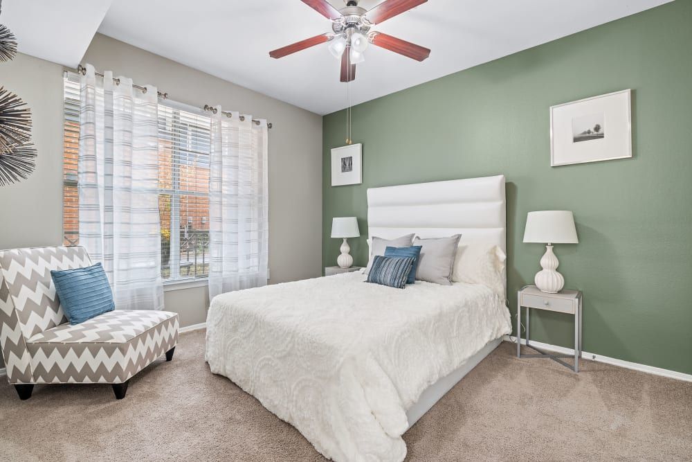a bedroom with a bed, chair, lamps, and a ceiling fan at Marquis on Gaston in Dallas, TX.