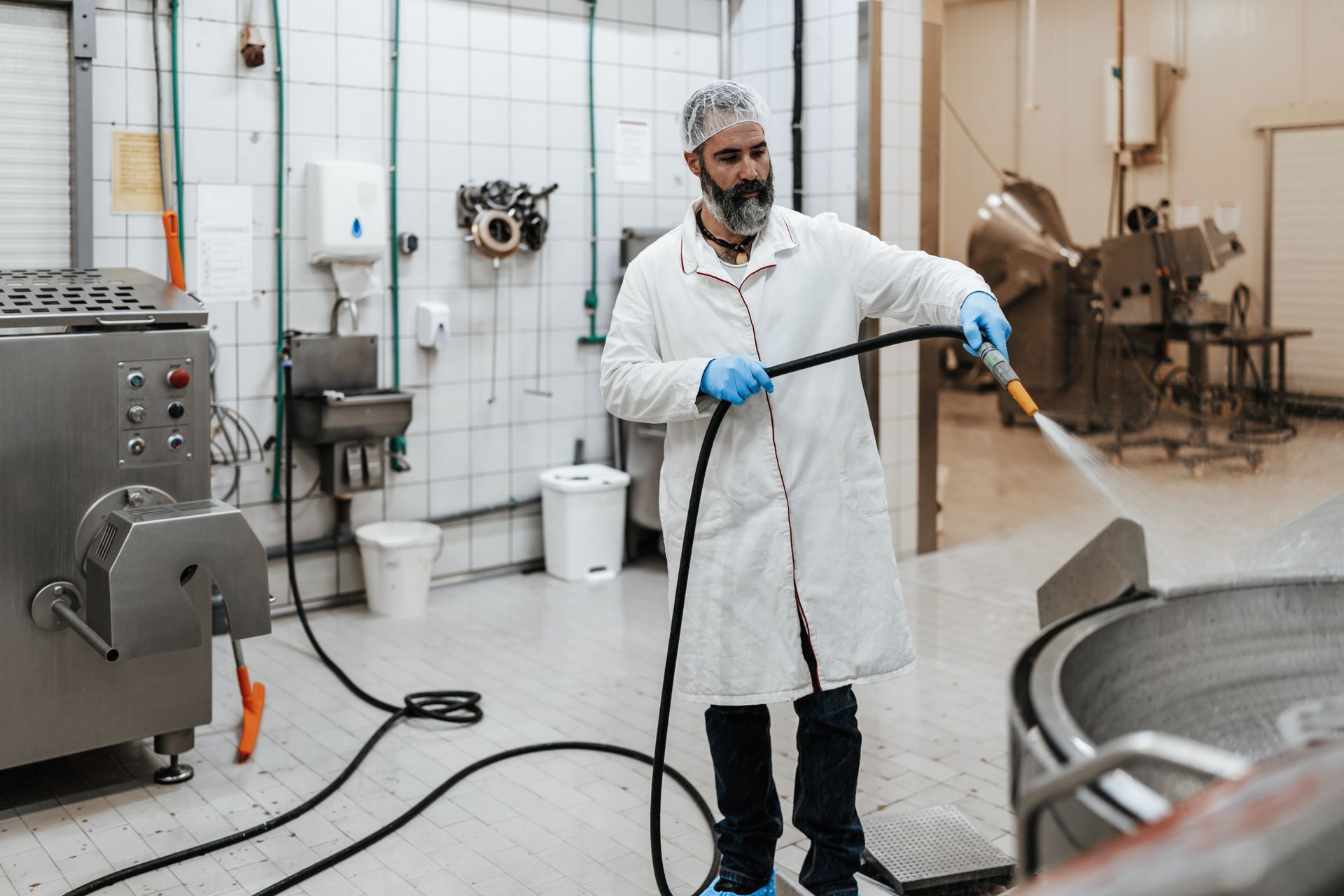 Un homme nettoie une machine avec un tuyau dans une cuisine.