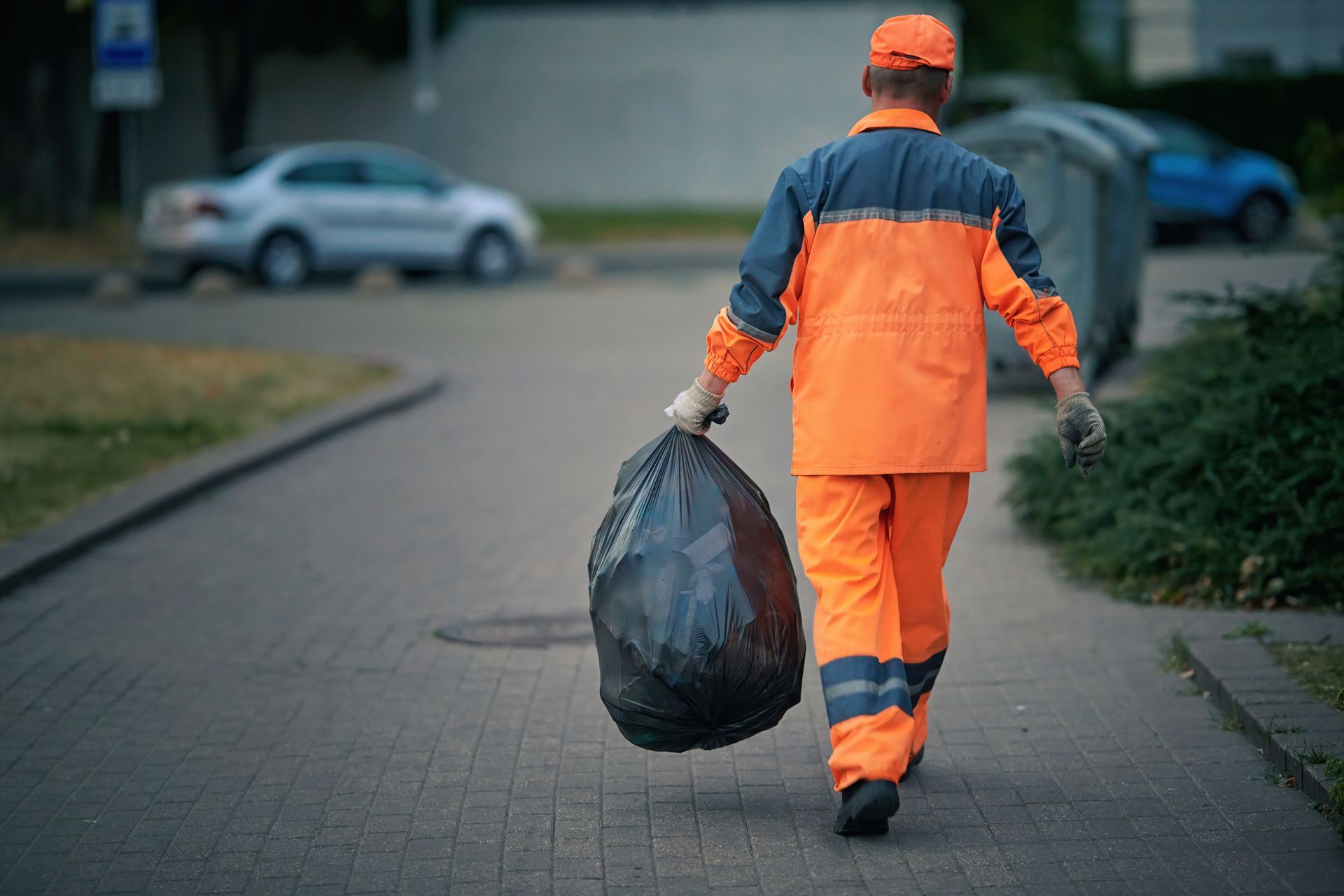 Un éboueur marche sur un trottoir en portant un grand sac poubelle noir.