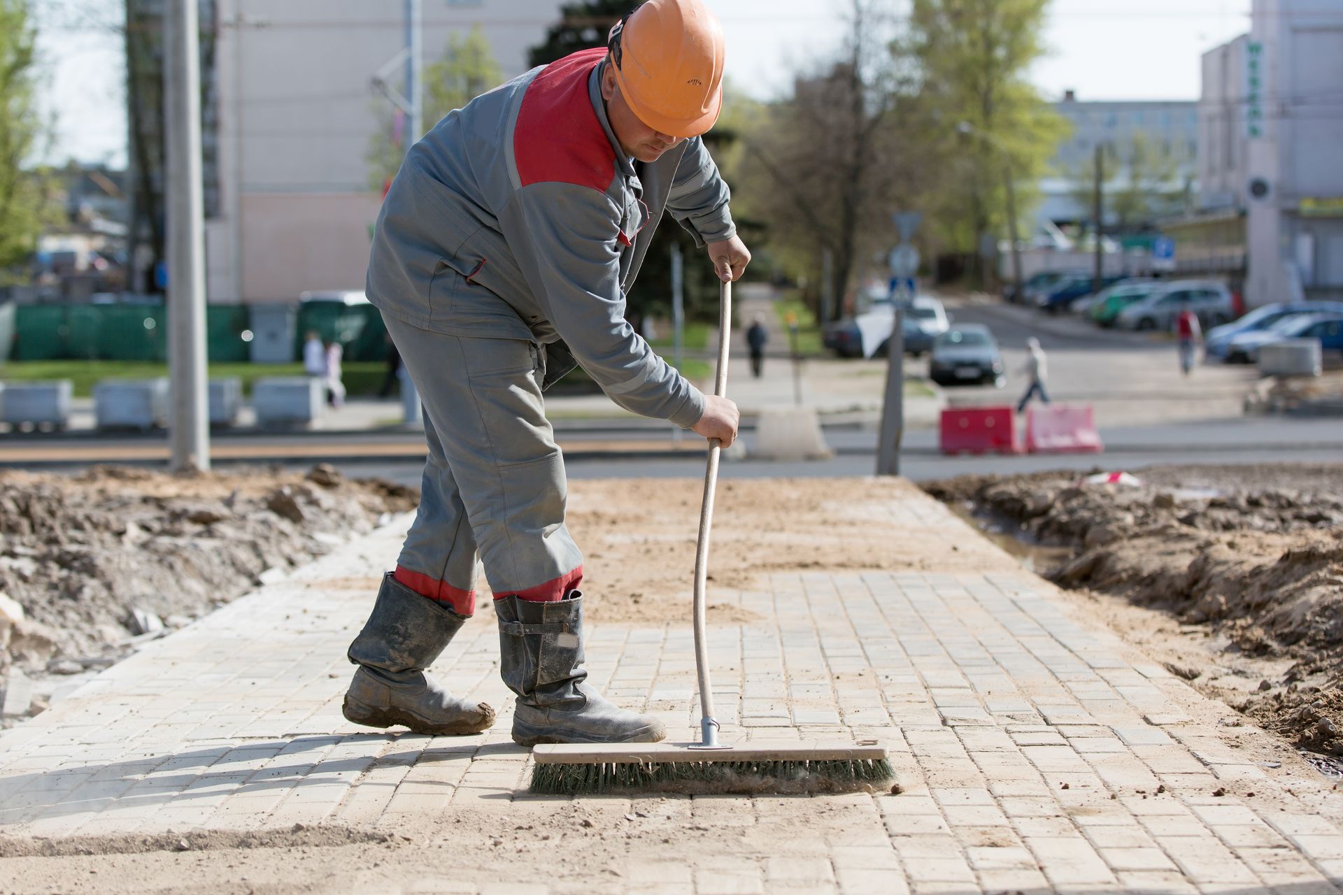Un ouvrier du bâtiment balaie un trottoir avec un balai.