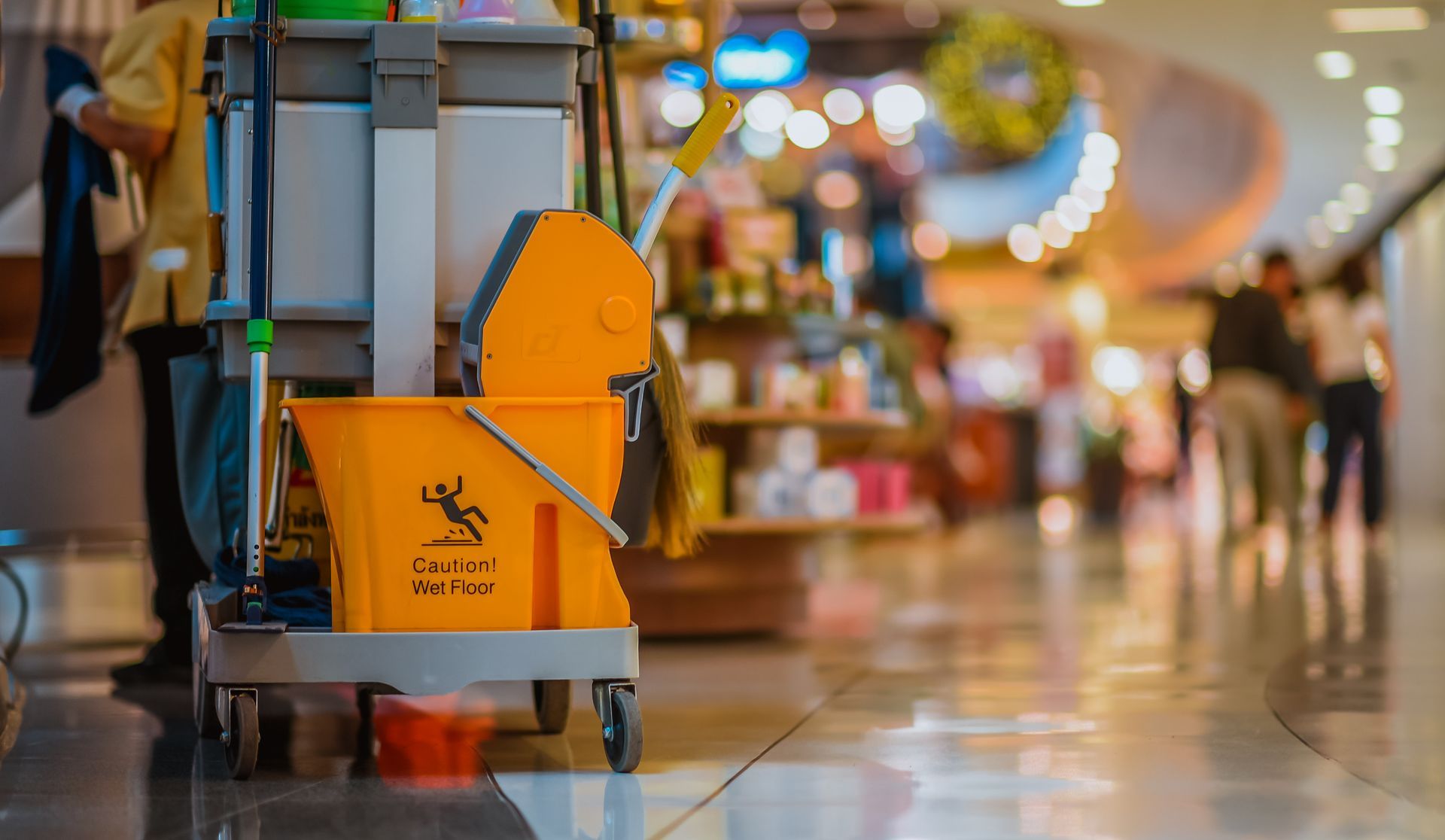 Un chariot de nettoyage avec un seau jaune et une serpillière dans un centre commercial.