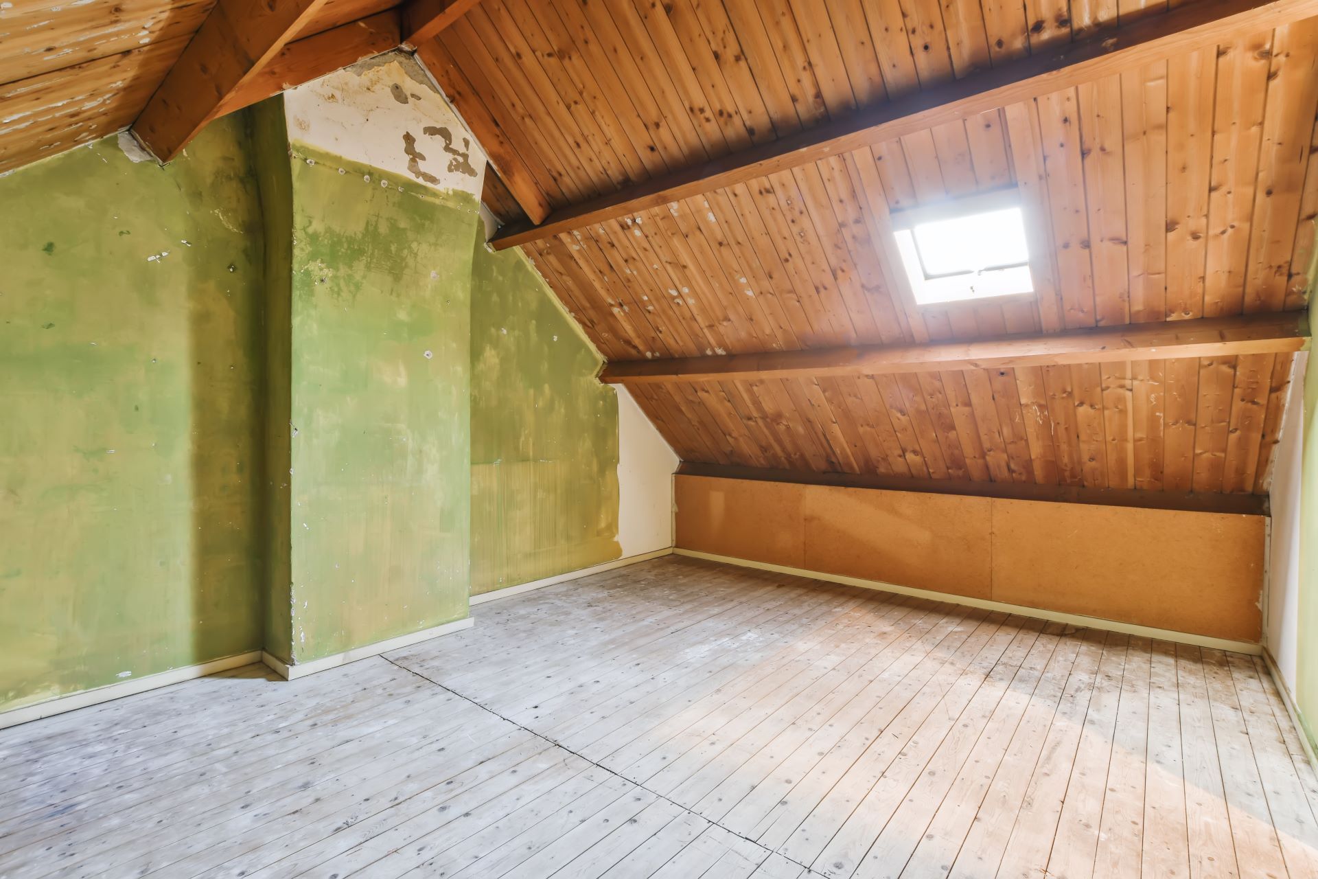 An empty attic with a wooden ceiling and a window.
