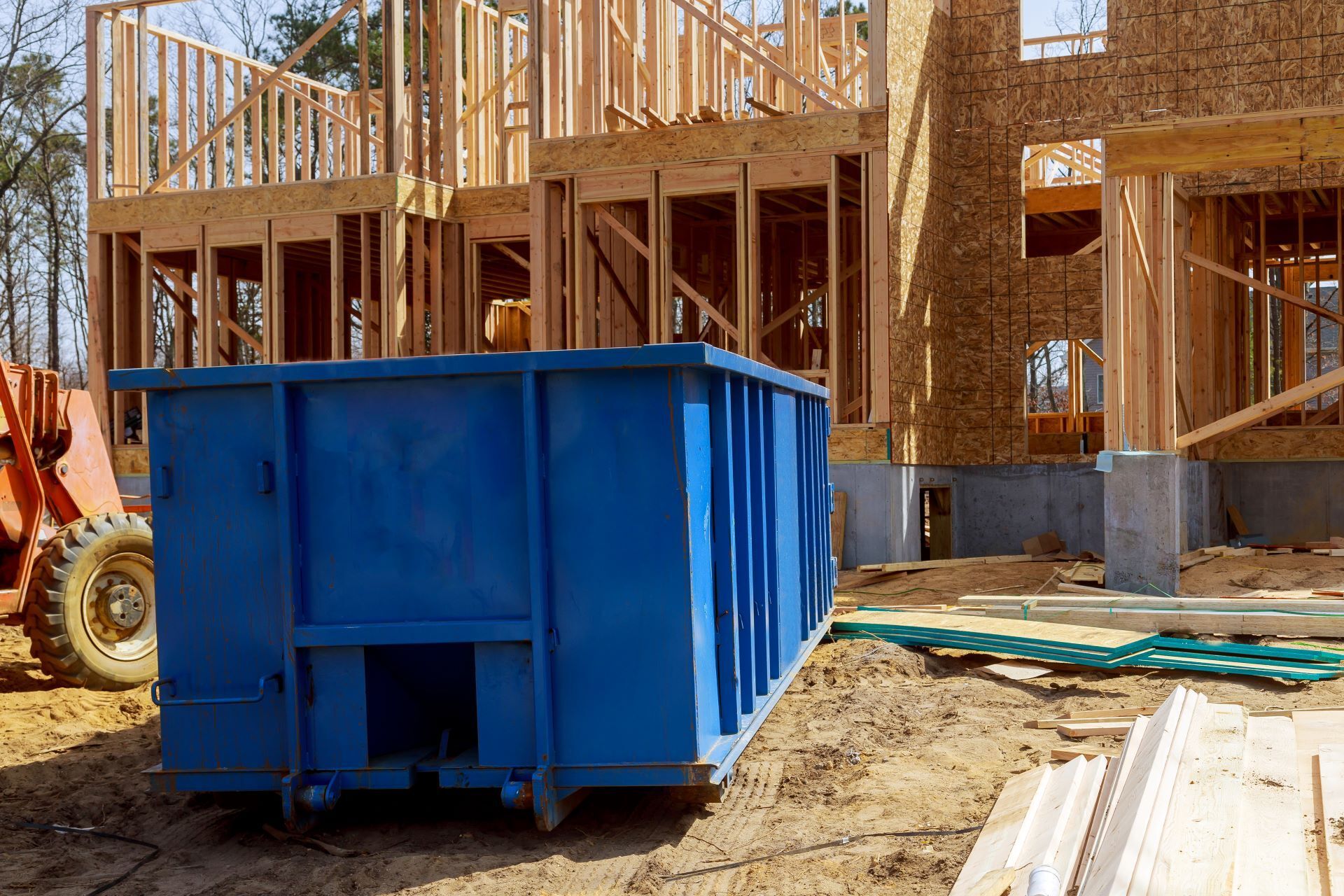 A blue dumpster is parked in front of a house under construction.