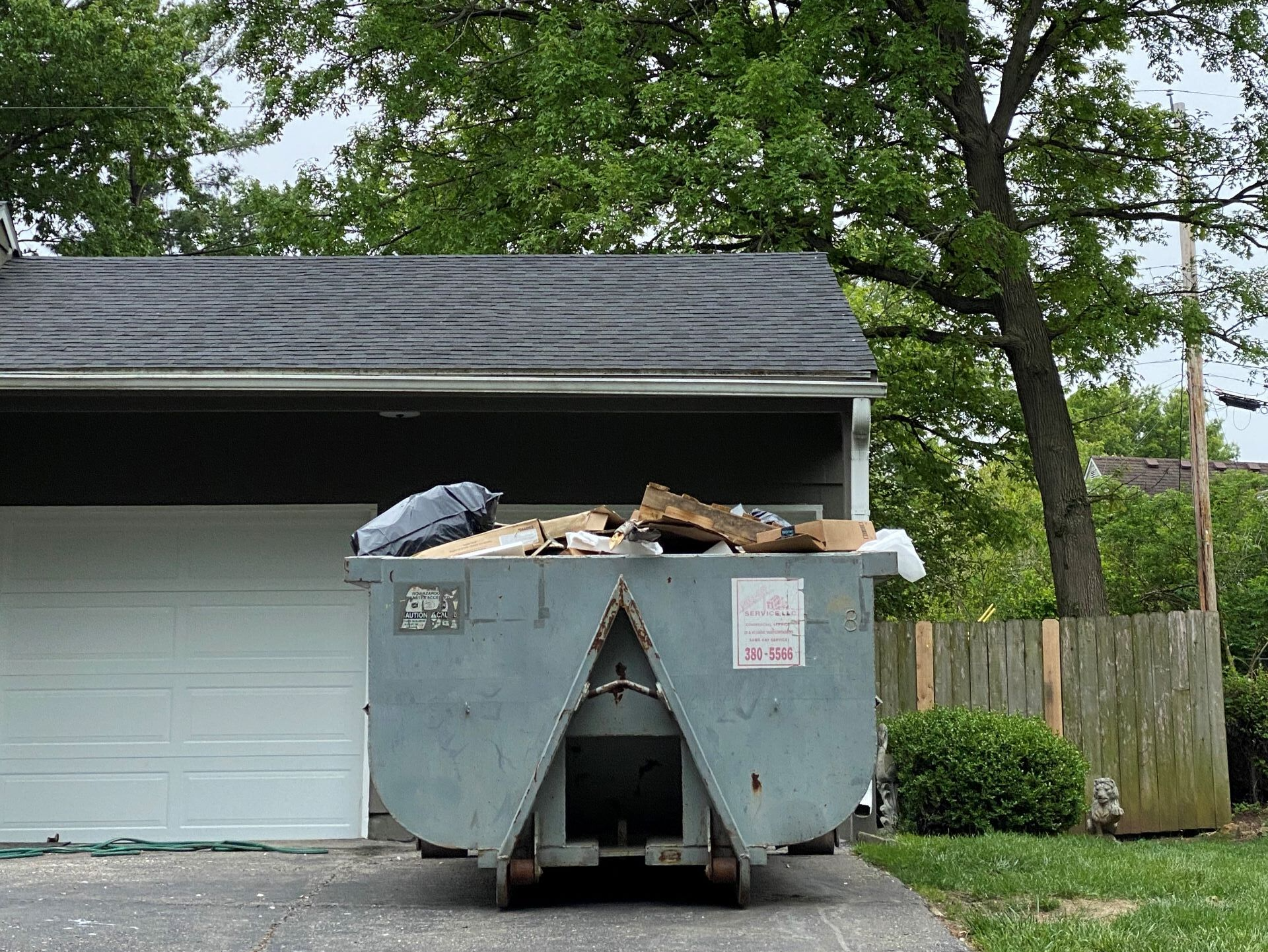 A dumpster filled with garbage is parked in front of a garage.