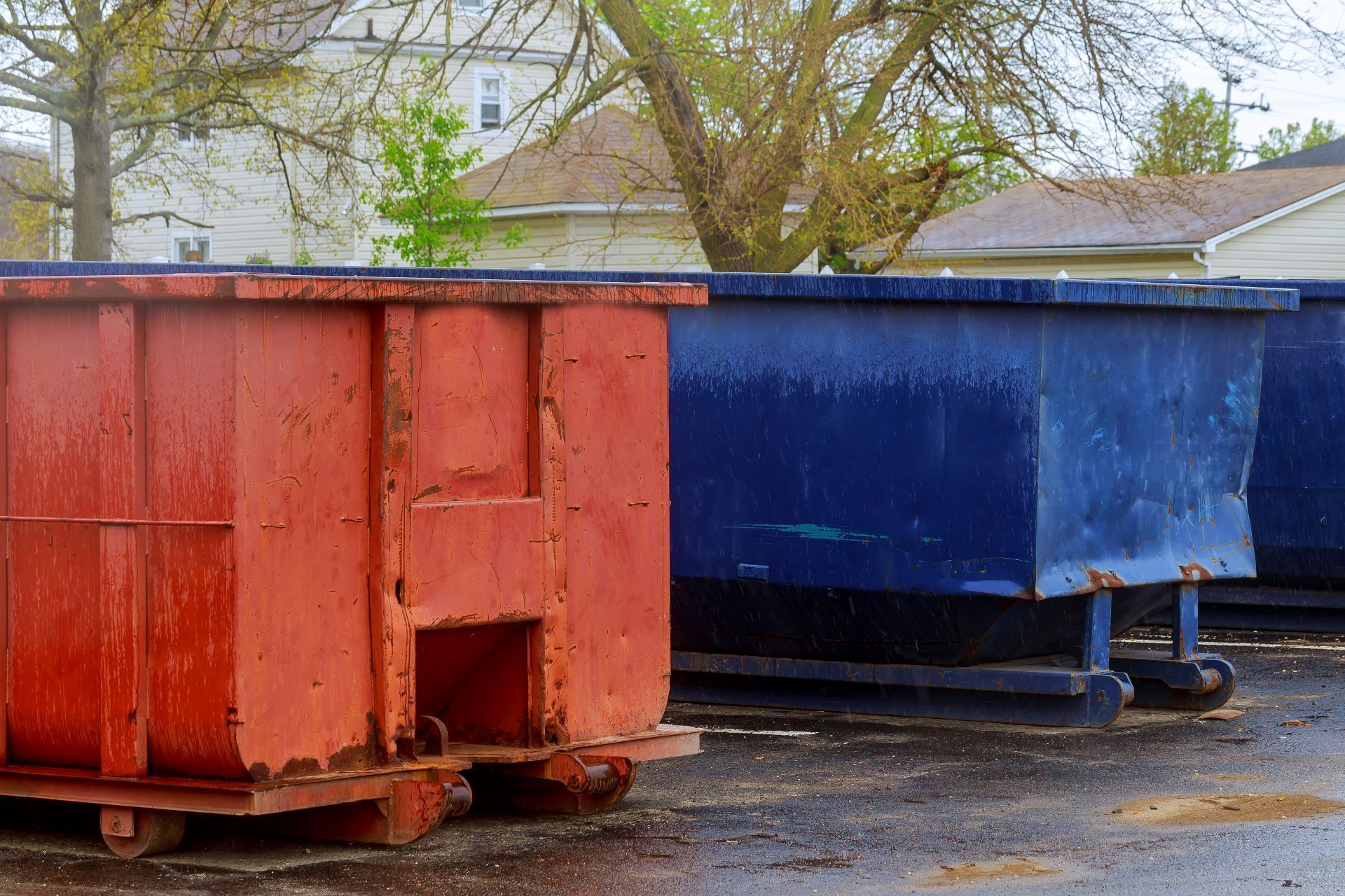 A red dumpster and a blue dumpster are parked next to each other in a parking lot.