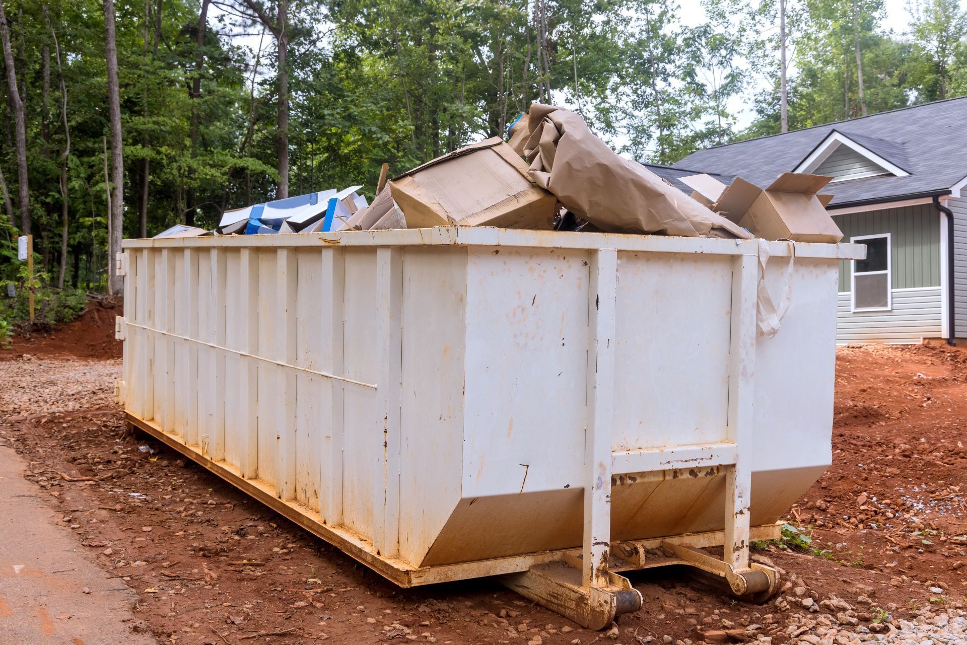 A large white dumpster filled with cardboard boxes is sitting in front of a house under construction.
