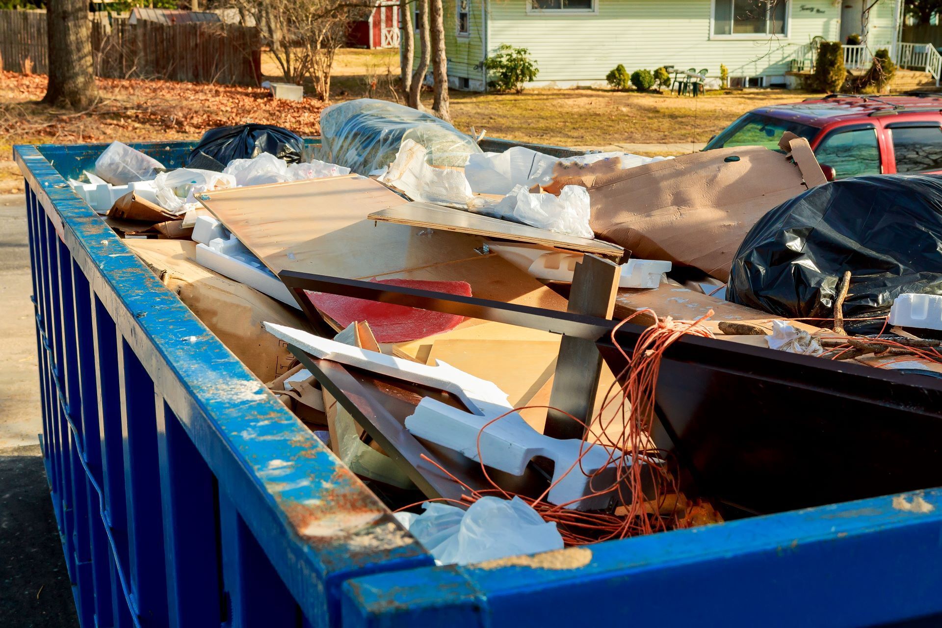 A blue dumpster filled with junk is parked in front of a house.
