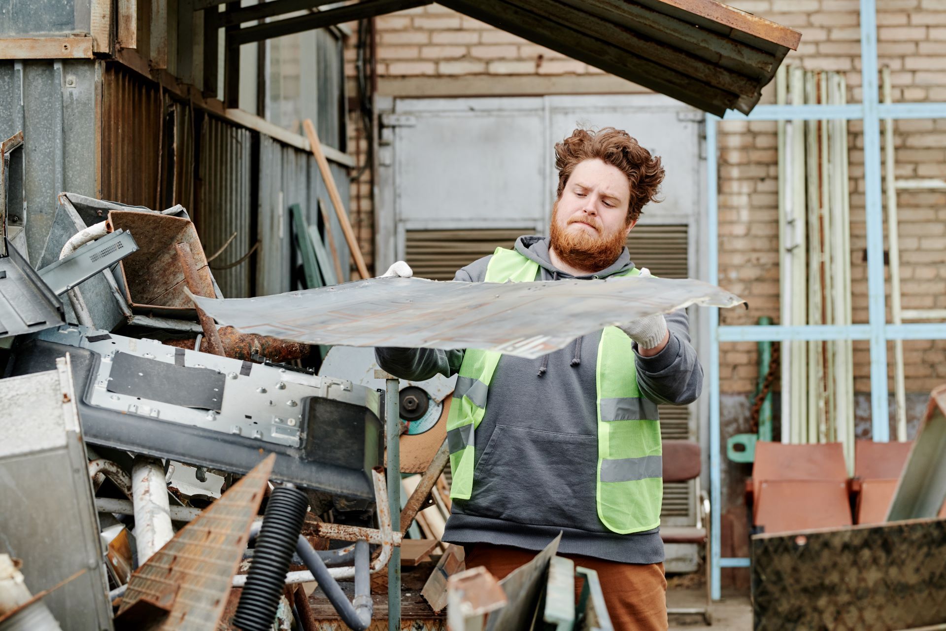 A man in a safety vest is cutting a piece of metal with a saw.